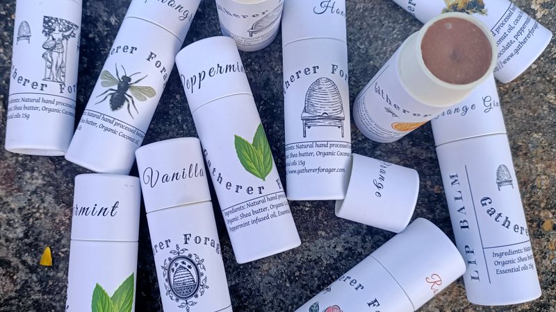 Gatherer Forager beeswax lip balms in illustrated cardboard tubes, laid out on stone