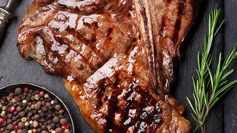 A grilled T-bone steak with cracked pepper and rosemary